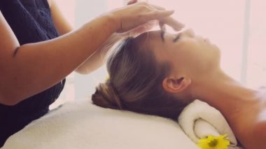 Lüks bir spa merkezinde masaj terapisti tarafından yüz masajı ve spa tedavisi için kaplıcaya uzanmış rahat bir kadın. Sağlık, stres atma ve gençleştirme kavramı.