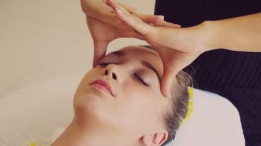 Lüks bir spa merkezinde masaj terapisti tarafından yüz masajı ve spa tedavisi için kaplıcaya uzanmış rahat bir kadın. Sağlık, stres atma ve gençleştirme kavramı.