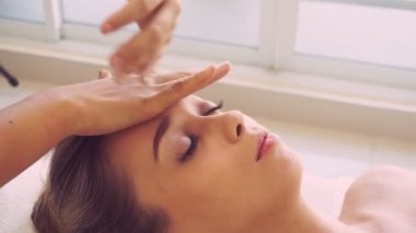 Lüks bir spa merkezinde masaj terapisti tarafından yüz masajı ve spa tedavisi için kaplıcaya uzanmış rahat bir kadın. Sağlık, stres atma ve gençleştirme kavramı.