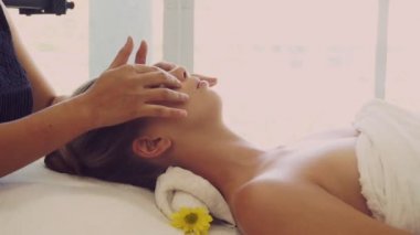 Lüks bir spa merkezinde masaj terapisti tarafından yüz masajı ve spa tedavisi için kaplıcaya uzanmış rahat bir kadın. Sağlık, stres atma ve gençleştirme kavramı.