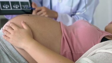 Mutlu hamile kadın, jinekolog doktoru hastanede ya da klinikte hamilelik danışmanlığı için ziyaret ediyor. Doktor, bebek ve anne sağlığı kontrolü için hamile karnı muayene ediyor. Jinekoloji konsepti.