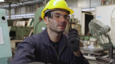 Fabrika işçisi, makine parçalarını incelerken taşınabilir radyodan konuşuyor.