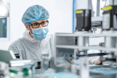 Yüz maskeli üretim hattı işçisi elektronik fabrikasında çalışıyor.