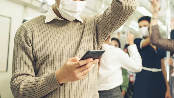 Trende cep telefonu kullanan gezgin yüz maskesi takıyor
