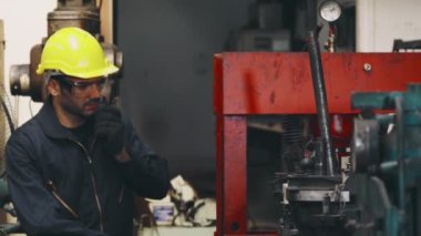 Fabrika işçisi, makine parçalarını incelerken taşınabilir radyodan konuşuyor.