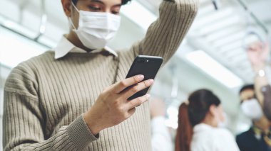 Trende cep telefonu kullanan gezgin yüz maskesi takıyor