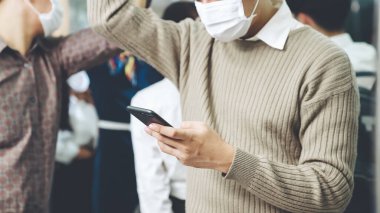 Trende cep telefonu kullanan gezgin yüz maskesi takıyor