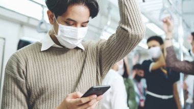 Trende cep telefonu kullanan gezgin yüz maskesi takıyor