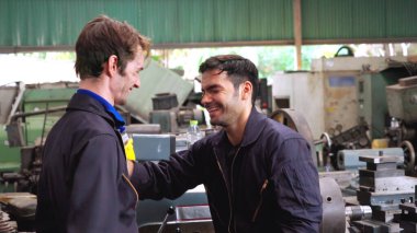 Yorgun fabrika işçileri mola verip fabrikada iş arkadaşlarıyla konuşuyorlar.