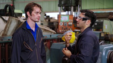 Yorgun fabrika işçileri mola verip fabrikada iş arkadaşlarıyla konuşuyorlar.