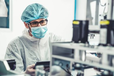 Yüz maskeli üretim hattı işçisi elektronik fabrikasında çalışıyor.