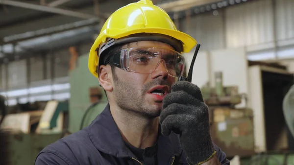 Pracownik fabryki rozmawia przez przenośne radio podczas kontroli części maszyn — Zdjęcie stockowe