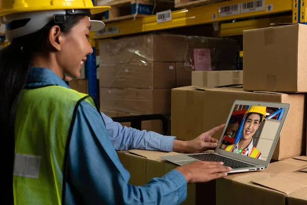 Warehouse staff talking on video call at computer screen in storage warehouse