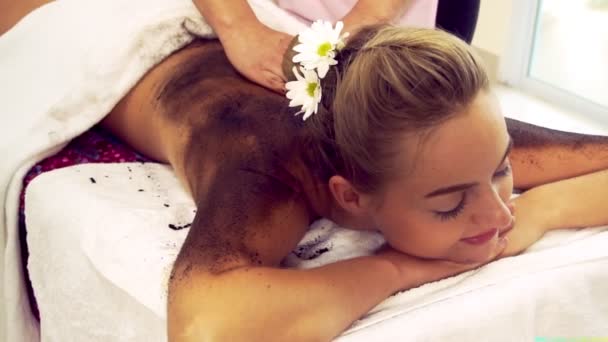 Entspannte Frau liegt auf Wellnessbett für Körperschrubbmassage mit traditionellen Kräutern — Stockvideo