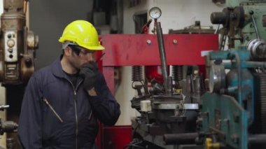 Fabrika işçisi, makine parçalarını incelerken taşınabilir radyodan konuşuyor.
