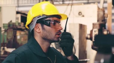 Fabrika işçisi, makine parçalarını incelerken taşınabilir radyodan konuşuyor.