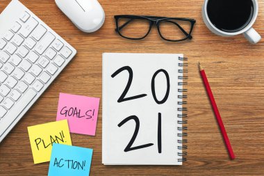 2021 Mutlu Yeni Yıl Kararları Hedef Listesi - Yeni yıl hedefleri ve kararları sıralaması hakkında el yazısıyla yazılmış bir not defteri ile iş yeri masası. Değişim ve kararlılık kavramı.