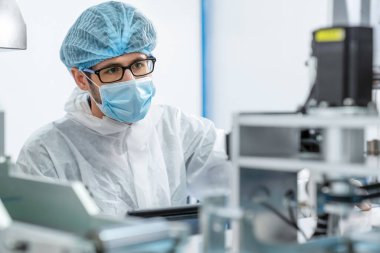 Yüz maskeli üretim hattı işçisi elektronik fabrikasında çalışıyor.