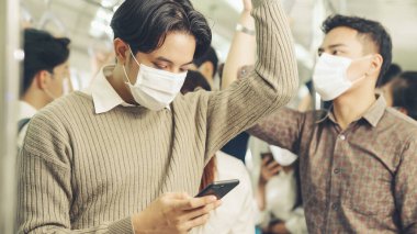 Trende cep telefonu kullanan gezgin yüz maskesi takıyor