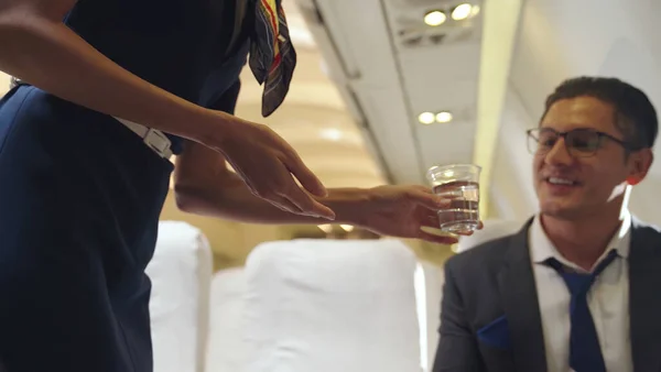 A tripulação da cabina serve água ao passageiro no avião — Fotografia de Stock