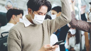Trende cep telefonu kullanan gezgin yüz maskesi takıyor