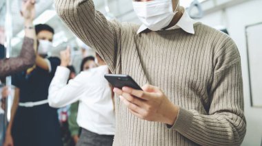 Trende cep telefonu kullanan gezgin yüz maskesi takıyor