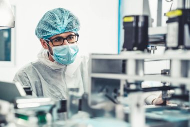 Yüz maskeli üretim hattı işçisi elektronik fabrikasında çalışıyor.