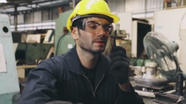 Fabrika işçisi, makine parçalarını incelerken taşınabilir radyodan konuşuyor.