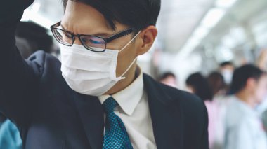 Yüz maskesi takan genç adam kalabalık bir metro treniyle seyahat ediyor.