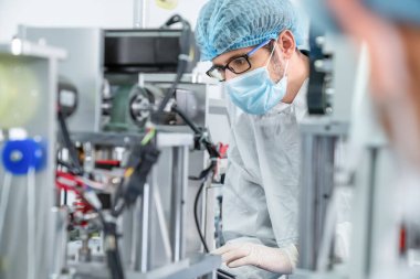 Yüz maskeli üretim hattı işçisi elektronik fabrikasında çalışıyor.