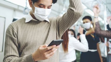 Trende cep telefonu kullanan gezgin yüz maskesi takıyor