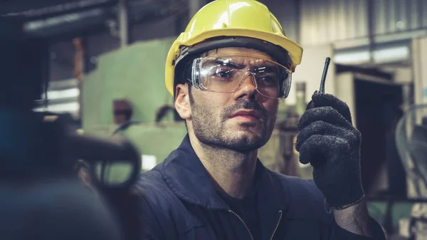 Tovární dělník mluví na přenosném rádiu při kontrole strojních dílů — Stock fotografie