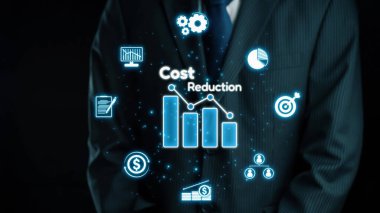 Takım elbiseli bir işadamı, dijital bir maliyet azaltma konsepti sunarak güvenle ayakta duruyor. Grafikler ve semboller modern işletmeler için finansal stratejileri ve performans ölçümlerini aydınlatır. Dörtgen