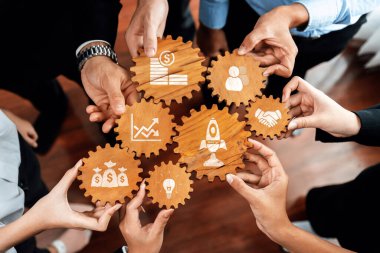 A group of professionals collaborates around wooden gears showcasing symbols of finance, networking, and innovation, emphasizing teamwork and strategic direction. Amity