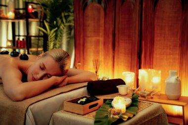 Lüks tatil köyündeki kaplıcalarda sıcak taş masajı, sıcak mum ışığı, spa bazalt taşı masajının keyfini çıkaran mutlu kadın müşteriler, rahatlatıcı bir sıcaklıkla vücudun üzerinde süzülüyorlar. Sessiz.