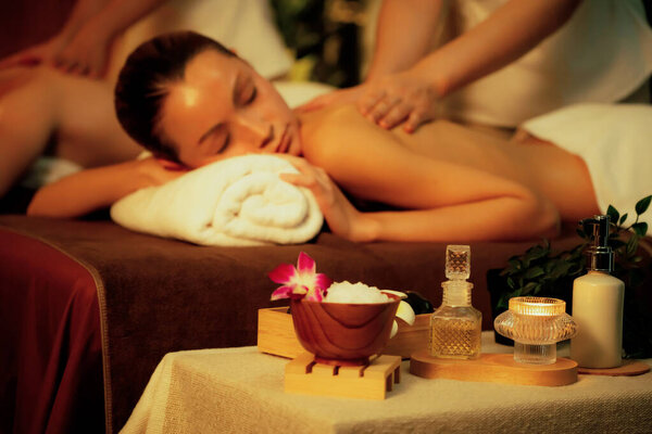 Кавказская пара клиентов, наслаждающихся расслабляющим антистрессовым спа-массажем и побаловать красотой отдых кожи в теплой свечи освещения окружающий салон спа на роскошный курорт или отель. Quiescent