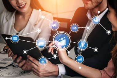 A group of business professionals engages in a collaborative discussion about digital strategy, showcasing technology graphics and analytics in a modern office environment. Tessel