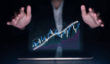A businessman uses advanced technology to analyze financial data through digital graphs in a dark office. This image represents growth, strategy, and modern finance. Impute