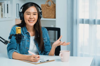 Sosyal medyada kulaklıkla canlı yayın yapan Asyalı sunucu modern stüdyoda yaşam koçluğu veya pazarlama dinleyicilerini selamlıyor. Taktik.