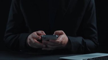 Bir kişi siber güvenliği temsil eden dijital simgelerle çevrili karanlık bir ortamda akıllı bir telefonla iletişim kurarak bilgiyi ve mahremiyeti korumanın önemini gösteriyor. Dörtgen