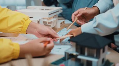 A diverse team of professionals collaborates in a modern office space, focusing on architectural designs and plans while engaging with scale models and technical drawings. SACTR