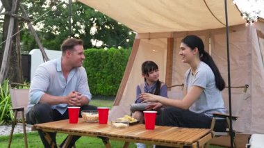 Aile hep birlikte bahçedeki kampta oturup yemek yiyor. Ebeveynler, genç nesil arasında iletişim kurmak ve zaman geçirmek için açık hava kamp faaliyetlerini kullanıyorlar. Uyumsuzluk.