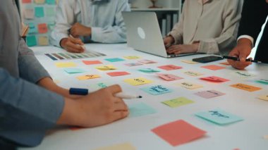 A vibrant office scene showcasing a collaborative brainstorming session with colorful sticky notes on a table, a laptop, and engaged team members sharing ideas. SACTR