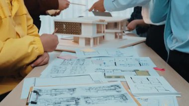 A vibrant collaborative workspace showcasing individuals engaged in discussing architectural designs, emphasizing teamwork and creativity through detailed blueprints and models. SACTR