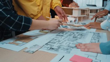 A dynamic scene showcasing teamwork in a modern office, with diverse hands collaborating over architectural blueprints and construction plans, emphasizing creativity. SACTR