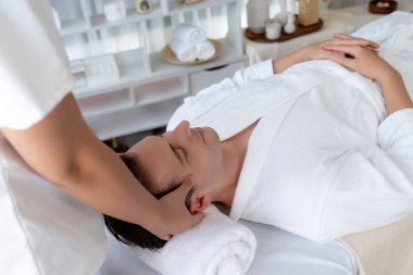 Beyaz adam stres önleyici kafa masajından ve lüks bir tatil beldesi veya otel spa salonundaki modern ışık ortamında yüz güzelliği eğlencelerini şımartmaktan hoşlanıyor. Sessiz.