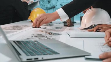 A group of professionals collaborates in a modern office setting, analyzing technical drawings and data with safety gear and laptops on a table, ensuring effective project management. SACTR