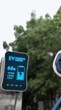 Doğal yeşil araba parkındaki ekolojik temiz enerji şarj istasyonundan gelen fütürist akıllı EV şarj aletinin şarj ettiği elektrikli araba. Alternatif enerji kullanan gelecekçi çevre dostu elektrikli araba. İnceleyin