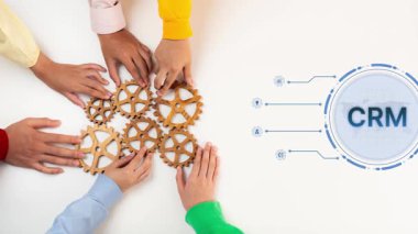 Diverse hands gather around wooden gears, symbolizing teamwork and collaboration in a business setting, with a digital CRM interface suggesting modern strategies. Raster