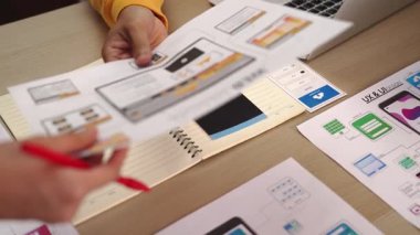 Mobil uygulama için kullanıcı arayüzü prototipini ofis çalışma alanındaki akıllı yöneticiye sunan mükemmel bir şirket çalışanı. UX UI tasarımcısı kağıt üzerinde simge tasarımının işlevini açıklıyor. Sinerjik